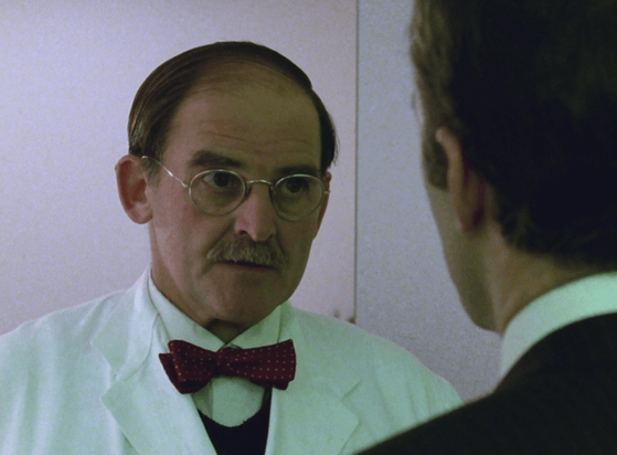 ChatGPT describes the image as "The image depicts a tense moment between two characters in a clinical or institutional setting, suggested by the white walls and the presence of a man in a white lab coat. The man in the lab coat, wearing glasses and a red bow tie with polka dots, appears serious and contemplative, likely a medical professional or scientist. He faces another man whose back is to the camera, indicating a private or confidential conversation. The scene suggests an exchange of important or sensitive information, reflecting the series' themes of conspiracy, investigation, and uncovering dark truths within bureaucratic and scientific environments."

BotOfDarkness, version 2.0.23.