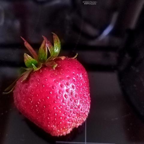 Nahaufnahme einer roten Erdbeere auf schwarzem Untergrund.
A close-up of a red strawberry on black underground.