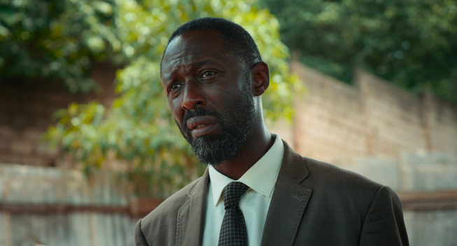 Thomas Ngijol dans le film Indomptables - en plan rapproché, de trois quarts face, portant costume et cravate.