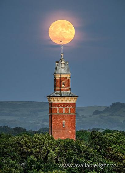 The moon, large in the sky above an ornate tower with a small domed roof. Trees surround the tower. The lightning conductor atop the tower "pierces" the centre of the moon.