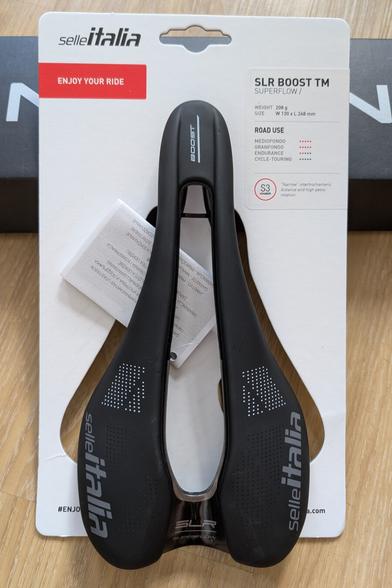 top down view on the  Selle Italia SLR Boost TM S3 saddle on the cardboard backing it came with. The white backing shows information about the intended use, dimensions and weight.