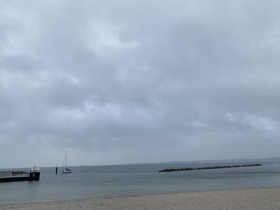 Ein Segelboot fährt unter Motor in den Hafen von Schilksee ein. Es nieselt, Laboe ist im Regendunst jenseits des Wellenbrechers vor dem Schilkseeer Strand kaum zu erkennen.