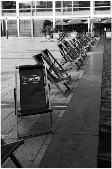 A row of deck chairs by a pool in Central Milton Keynes shopping centre. One chair is at 90⁰ too the rest.