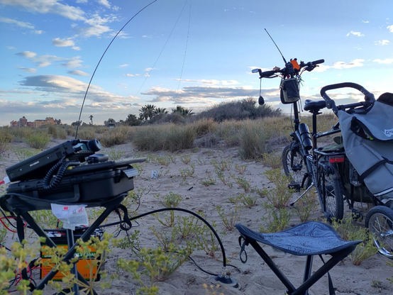 At the left side, a ham radio at the top of a chair, on the right side, a bycicle with a trailer in the sape of a shopping cart attached. Behind all of that, a fishing rod bending to sustain a wire in the air in a inverted vee shape.