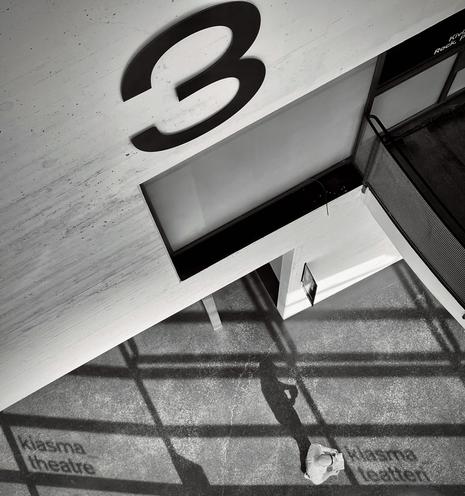 A high viewpoint of a corridor with a large number 3 on the wall and a person casting a shadow over the words "Kiasma Theatre."