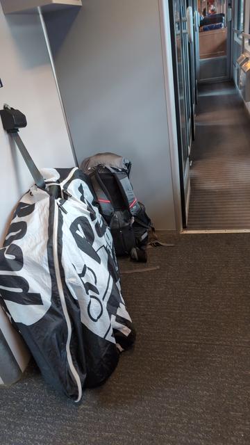 Ein in eine Transporttasche verpacktes Rennrad und ein kleiner Rucksack stehen in einem Bahnwagenvorraum.