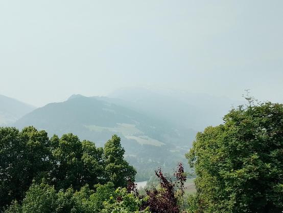 Berge im Dunst, davor grüne Bäume und Wiesen
