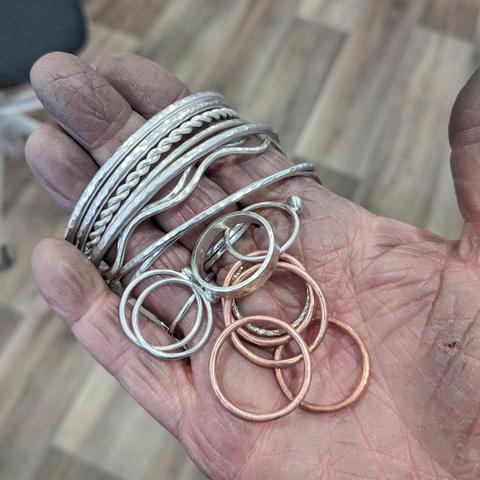 A very mucky outstretched hand holding a selection of silver and copper rings and bracelets
