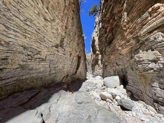 A hiker looks tiny standing between two towering canyon walls known as Devil's Hall in Guadalupe Mountains National Park, Texas.