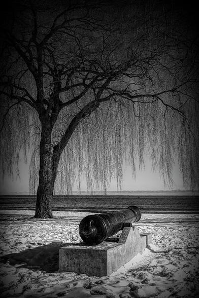 A lone cannon overlooks Lake Ontario in Marie Curtis Park, Toronto on a bright winter day, captured in black and white.