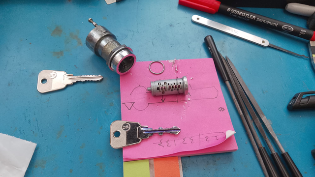 A disassembled wafer tumbler lock and two hand-filed (badly) keys. One operates the lock, but only one way up.