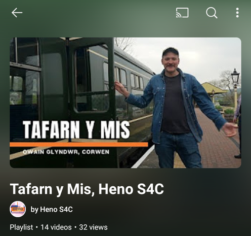 'Tafarn y Mis' playlist on Heno's YouTube Channel. The playlist's accompanying photo has Welsh Whisperer standing next to a heritage railway carriage for an episode visiting Gwesty Owain Glyndŵr, Corwen. Playlist currently contains 14 videos.