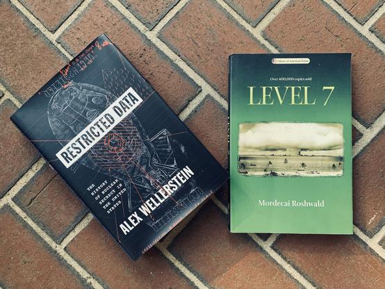 Pictured are the books Restricted State: The History of Nuclear Secrecy in the United States, a nonfiction book by historian Alex Wellerstein, and the classic science fiction novel Level 7 by Mordecai Roshwald (with cover art depicting a mushroom-shaped cloud). Both sit on a brick walk.
