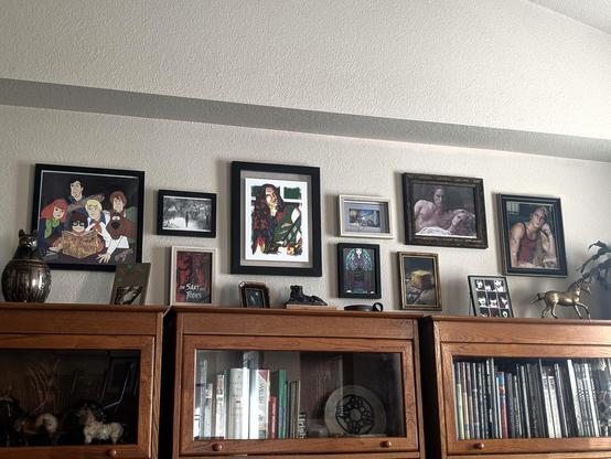 A collage of framed and matted art prints hanging on a wall above four oak barrister's bookcases.