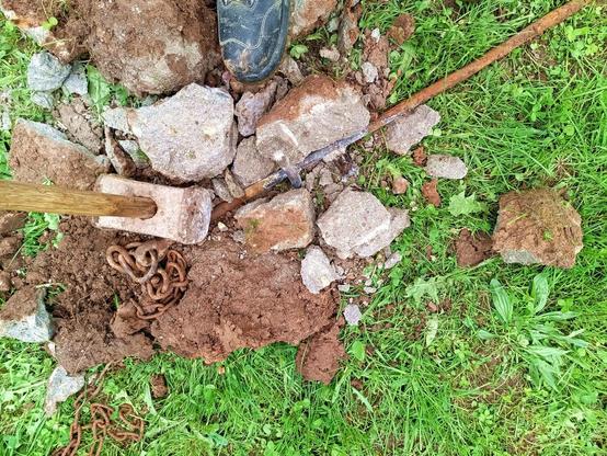 The concrete cast smashed to pieces with a big steel mallet (about the size of my boot) and revealing the crossbars welded to the thick steel rod. A piece of rusty chain and swivel are attached to a ring at the top.