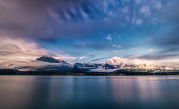 Langzeitaufnahme von interessanten Wolkengebilden um Berge an einem See.