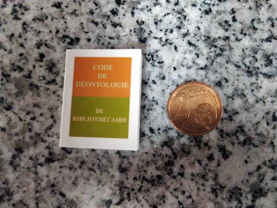 Un minuscule exemplaire du « Code de déontologie du bibliothécaire ». À côté de lui, une pièce de 2 centimes d’euro, à peine plus petite.