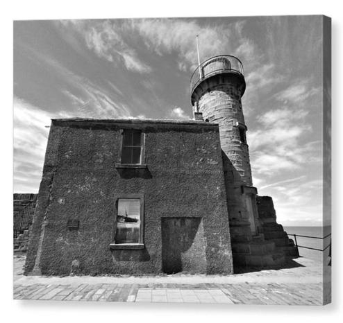 Black and white photograph of an old square building alongside a small lighthouse at the end of a pier.  The image is shown printed upon a box canvas.