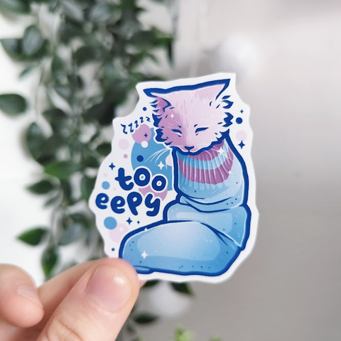 Hand holding up a sticker of a kitty sleeping in a sock titled "too eepy"