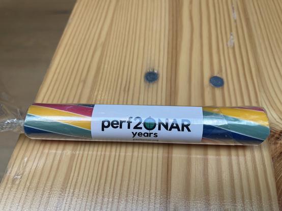 Colourful rock packaged with a label reading "perf2ONAR years." The candy has pink, yellow, teal, and blue stripes, resting on a wooden bench.