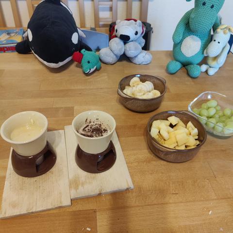 Der Mensch macht sich Schokofondue. Orca Panda, Wal mit Hut, Eisbär Theo sowie die Drachen Tabaluga und Arktos gucken mit Sicherheitsabstand zu.