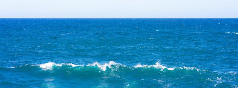 Blue ocean with small waves breaking on the surface under a clear sky, horizon line visible where the sea meets the sky.