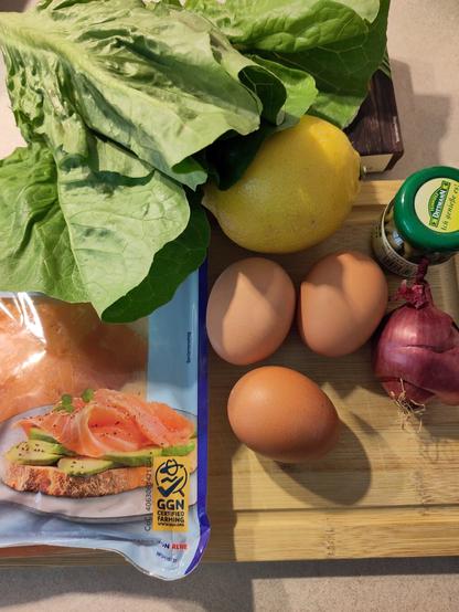 Ein paar der Zutaten auf einem Holzbrett. darubter der Salat, Räucherlachs, gekochte Eier, Kapern, Zwiebel.
die Zitrone, die hier auch bereit lag, habe ich dann doch nicht verwendet.