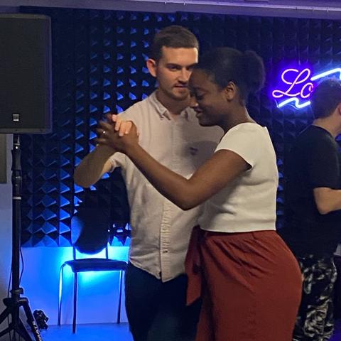 A woman smiles as she leads a taller man around her in a turn.