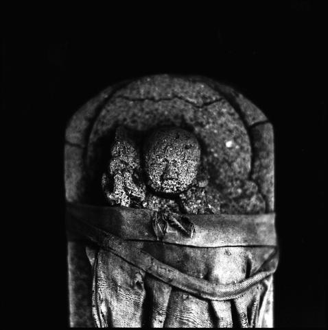 black and white, high contrast, photograph of a small buddhist status. a tattered and frayed piece of cloth is wrapped around the statue.