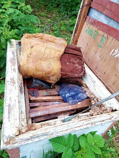 Same box with the cushions pulled back. There's a mess of cushion stuffing gnawed and dragged around by rodents. The frames are loose and misaligned. Some old comb is visible on them. There's what looks like a wooden box thrown in at an angle, too.