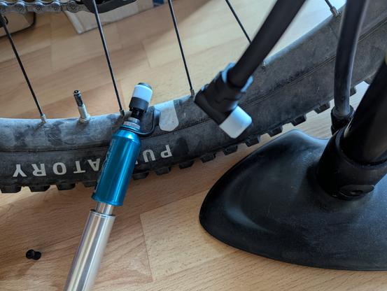 Hinterrad eines Fahrrads. Man kann Purgatory auf dem Reifen lesen. Das Ventil ist ein neues Clik. Auf der Felge liegt eine Pumpe mit Clik Adapter. Rechts sieht man einen Teil einer Standpumpe. Auch da ist am Ende ein valve Adapter verbaut