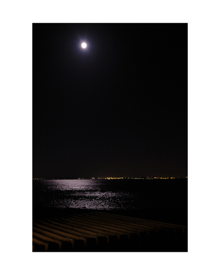 view over tejo river by night, moon shining from above with scattered reflexions in black water