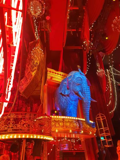 Side stage of the Moulin Rouge musical, consisting of small bar, with a blue elephant on its roof. To the left is a small balcony where people could sit, to the right is a cage-like structure where someone could stand and dance in.

Overall coloring is red and gold, with lots of small decorations and lights.