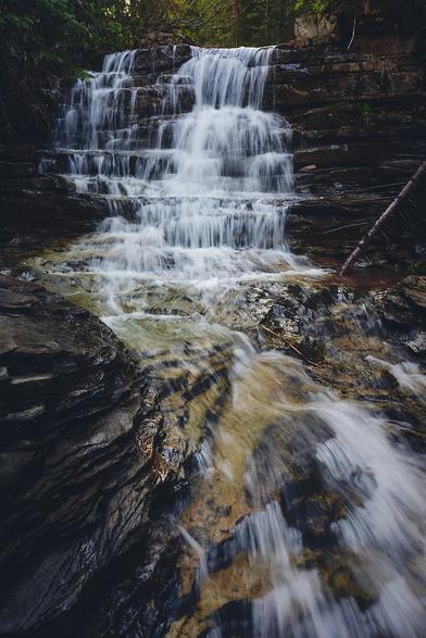 A cascading waterfall flows over layered rocks in a forest setting.