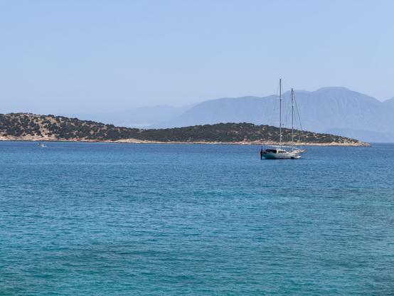 A sailboat anchored near a rocky island in the clear blue sea in Crete.