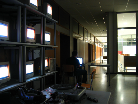 CRT monitors in a corridor with a person sitting in front of it.
