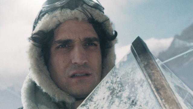 Filmstill, ein Pilot in einer alten Propellermaschine, im Hintergrund sind Berge zu sehen.