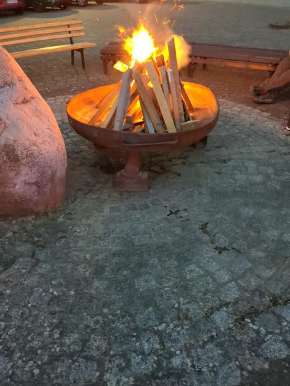 A fire burning on the market place of a village. Benches around the fire place.