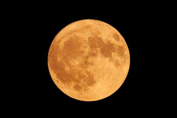 Photograph of a large full moon, tinged creamy yellow by wildfire smoke.