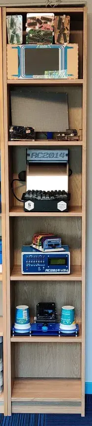Tall thin Billy Bookcase from IKEA filled with RC2014 exhibits usually on display at tech events. From the top down there are 4 Mini II Picasso kits. An RC2014 branded HDMI screen, a Pixel Purse screen with the Mini After Dark next to it and a one-off Picasso prototype. Below that is the RCade then the RC2014 Pro Pride, an RC2014 Zed in a Blue Box enclosure, and finally a Mini II with Dual Paddle Analogue Module and NeoPixel Matrix display in the Pot Noodle based Etch-a-Sketchy enclosure.