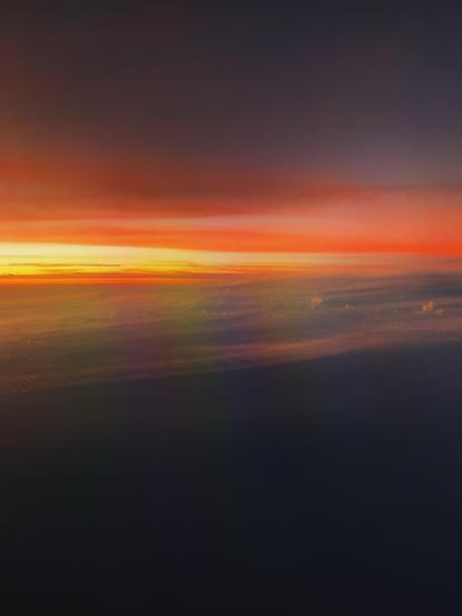 A dramatic sunset over the horizon, featuring vibrant shades of orange, red, and purple blending into the darkening sky. Soft clouds are visible, bathed in the warm glow of the setting sun.