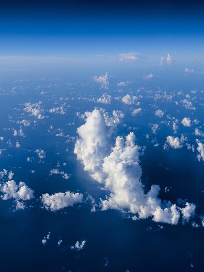 Aerial view of fluffy white clouds scattered over a deep blue ocean, with a clear sky above.