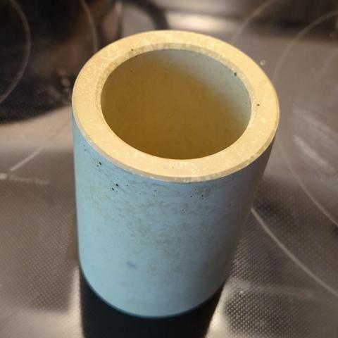 A pastel yellow cup with thick walls, on a black background (a glass stovetop).