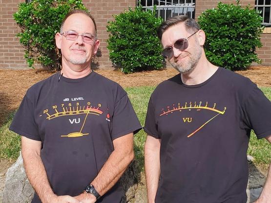 Two middle aged dudes standing in the sun wearing very similar black t-shirts with VU meters depicted
