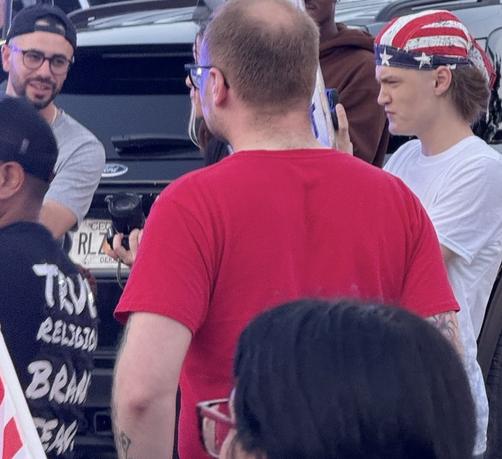Two men talking, David Khait on left and unidentified man in american flag bandana on right