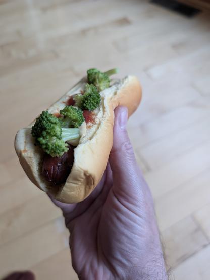 A hotdog in a bun, topped with broccoli