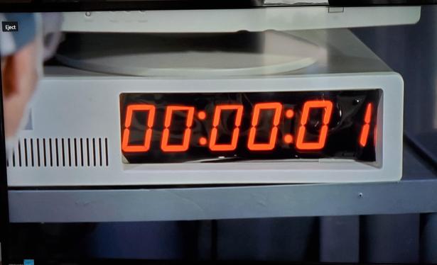 A picture of a TV showing an IBM PC case with a six digit seven-segment display where the floppy drives should be 

The case is the early 5150 or 5160 style case with room for two full height floppy drives. The display reads 1 second
