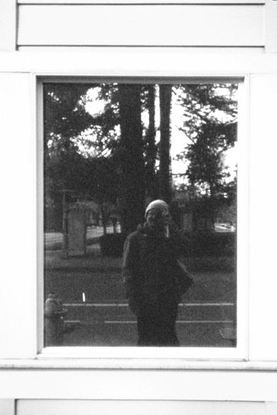 A black and white photo of a man taking his own picture in the reflection in a window.