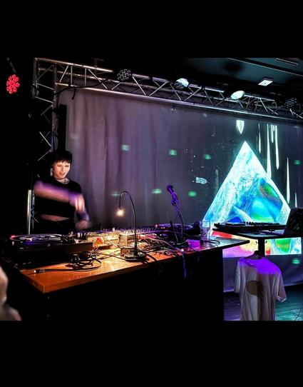 Smiling girl about to press a button on some fancy dj equipment next to a psychedelic picture of a crystal