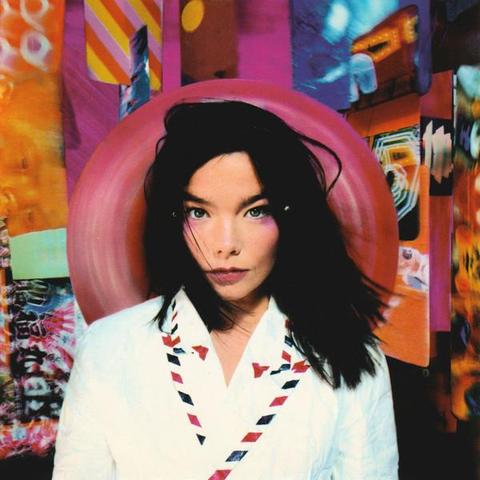 A woman with long black hair and a white shirt stares into the camera. All on a colourful background.